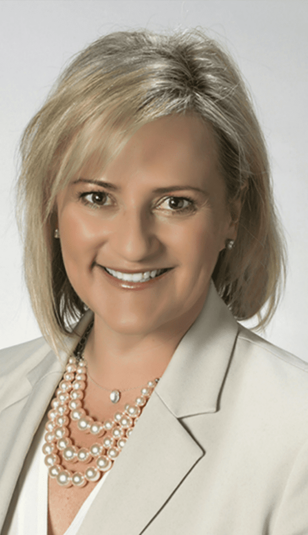 A woman with blonde hair wearing pearls and a white jacket.